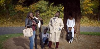 cinco pessoas, todas negras, posam em cena do documentário; estão sob uma árvore fazendo gestos e olhando um para cada lado