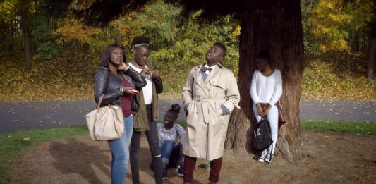 cinco pessoas, todas negras, posam em cena do documentário; estão sob uma árvore fazendo gestos e olhando um para cada lado