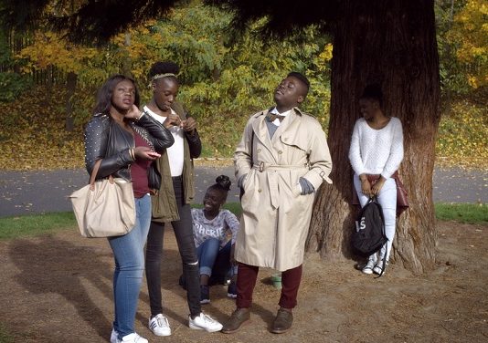 cinco pessoas, todas negras, posam em cena do documentário; estão sob uma árvore fazendo gestos e olhando um para cada lado