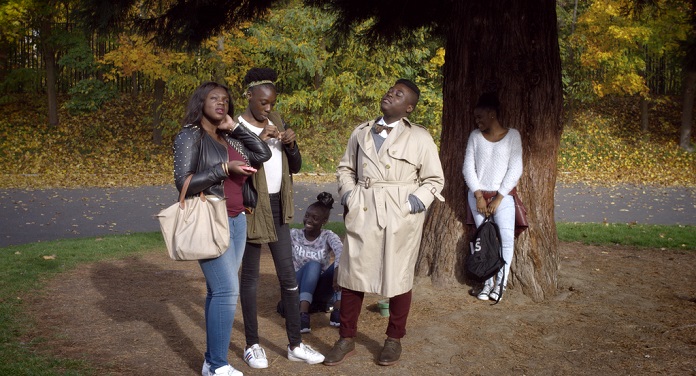 cinco pessoas, todas negras, posam em cena do documentário; estão sob uma árvore fazendo gestos e olhando um para cada lado