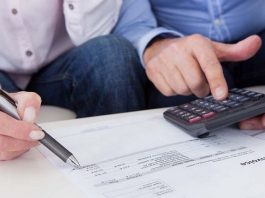 duas pessoas observam folhas com números e cifras com calculadora e caneta na mão