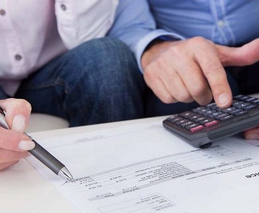 duas pessoas observam folhas com números e cifras com calculadora e caneta na mão