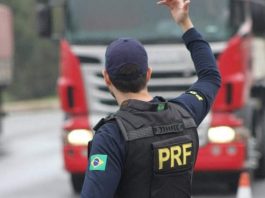 agente da prf visto de costas com uniforme da corporação gesticula com o braço direito para caminhão na estrada