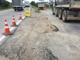 trecho de areia entre duas vias de asfalto com sinalização de cones e caminhões estacionados