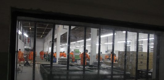 vista através de uma janela com grande de detentos uniformizados trabalhando em um salão