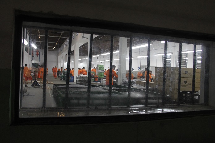 vista através de uma janela com grande de detentos uniformizados trabalhando em um salão