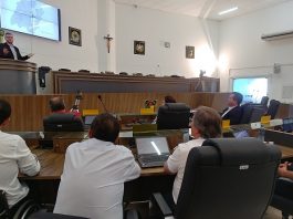 homem fala na tribuna da câmara de palhoça para alguns vereadores sentados, que observam