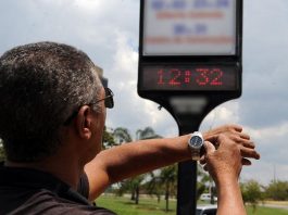 homem ajusta relógio de pulso olhando para relógio em painel na rua