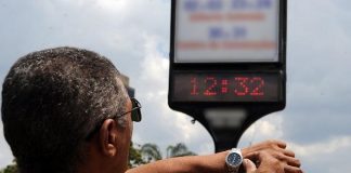 homem ajusta relógio de pulso olhando para relógio em painel na rua