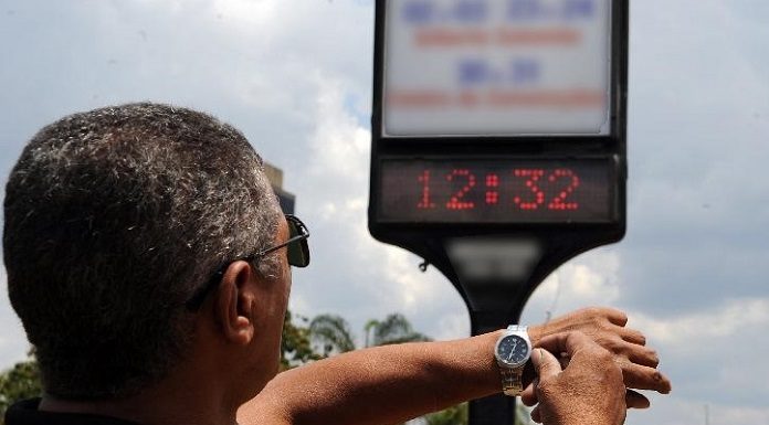 homem ajusta relógio de pulso olhando para relógio em painel na rua
