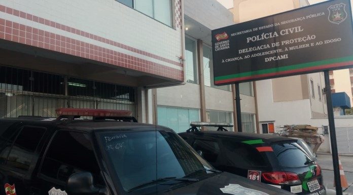 fachada e placa da delegacia, com duas viaturas estacionadas na frente