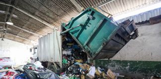 caminhão de lixo abre a parte traseira despejando grande quantidade de material reciclável em galpão