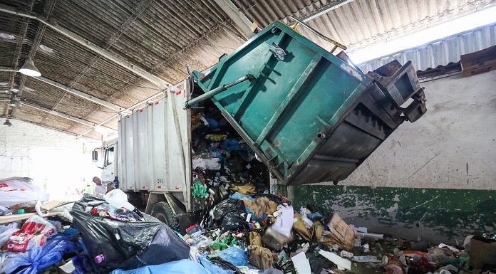 caminhão de lixo abre a parte traseira despejando grande quantidade de material reciclável em galpão