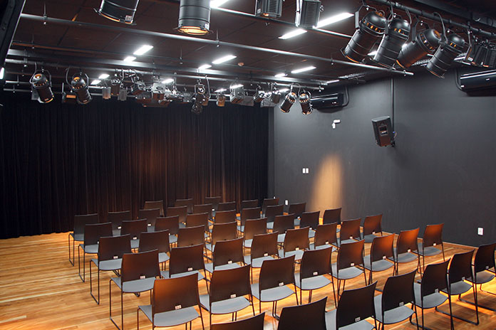 cadeiras pretas no auditório pouco iluminado, com uma cortina preta à frente