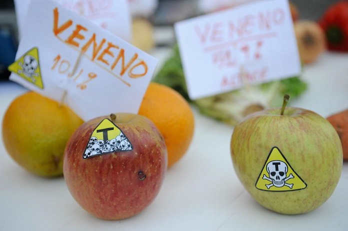 maçãs e laranjas sobre uma mesa com adesivos de risco de morte e plaquinhas de veneno
