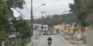 foto tirada no meio da rua onde há uma moto passando e obras no acostamento