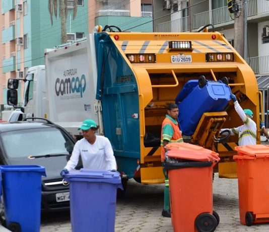 trabalhadores da comcap mexem em latões de lixo atrás de um caminhão de lixo, parado no meio de uma rua