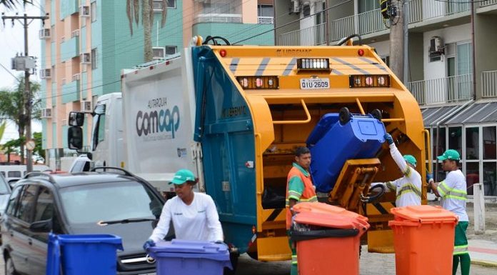 trabalhadores da comcap mexem em latões de lixo atrás de um caminhão de lixo, parado no meio de uma rua