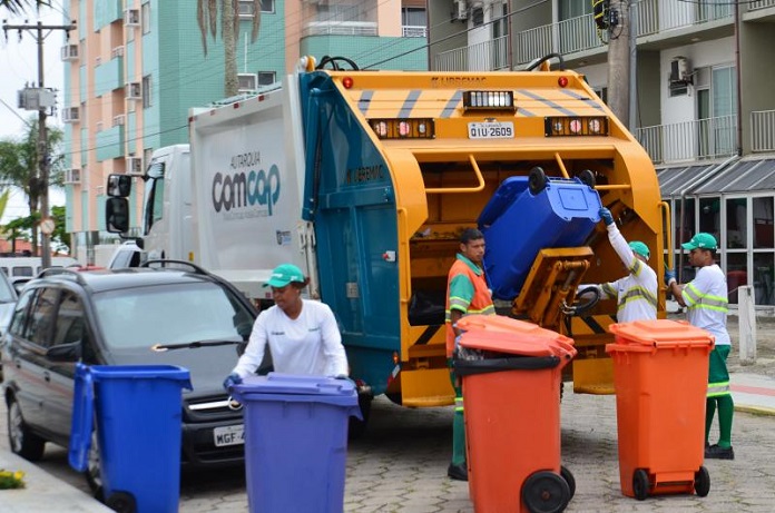 trabalhadores da comcap mexem em latões de lixo atrás de um caminhão de lixo, parado no meio de uma rua