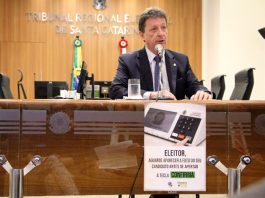 desembargador fala ao microfone numa bancada do tribunal, com um pequeno cartaz da urna eletrônica à frente