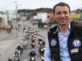 foto de moisés em cima de um caminhão, usando colete e adesivos do partido; há uma fila de motos que o acompanhando ao fundo na rua