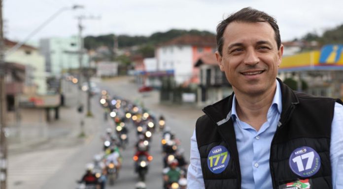 foto de moisés em cima de um caminhão, usando colete e adesivos do partido; há uma fila de motos que o acompanhando ao fundo na rua