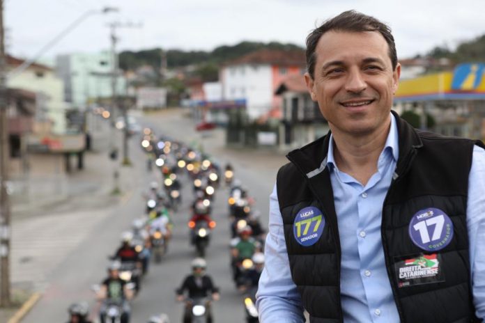 foto de moisés em cima de um caminhão, usando colete e adesivos do partido; há uma fila de motos que o acompanhando ao fundo na rua