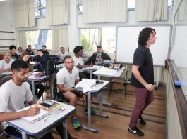 sala de aula com diversos homens sentado nas carteiras e professor olhando para o quadro