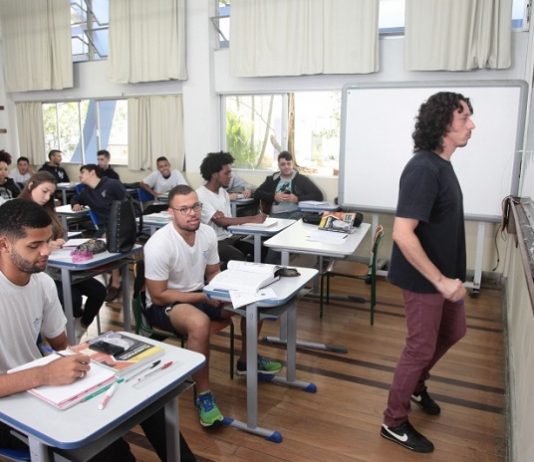 sala de aula com diversos homens sentado nas carteiras e professor olhando para o quadro