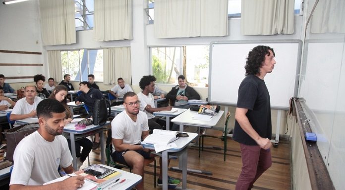 sala de aula com diversos homens sentado nas carteiras e professor olhando para o quadro