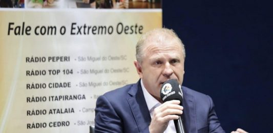 merisio fala com um microfone em uma mão e gesticula com outra