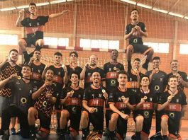 jogadores posam na quadra perfilados exibindo as medalhas e o troféu está no chão à frente da equipe