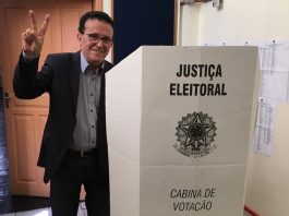 hélio faz sinal de vitória para a câmera ao lado da cabine de votação