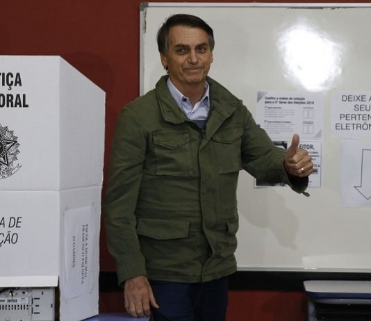 bolsonaro faz sinal de positivo ao lado de cabine eleitoral