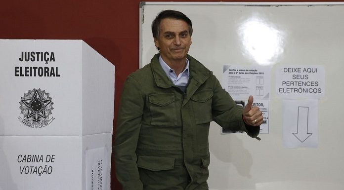 bolsonaro faz sinal de positivo ao lado de cabine eleitoral