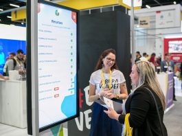 duas mulheres conversam entre si à frente de um grande tela em uma feira