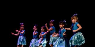 seis meninas com fantasias iguais dançam sorridentes lado a lado em um palco