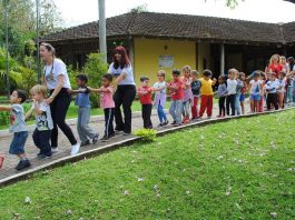 alunos e professoras fazem um trenzinho em área esterna com gramado da escola do meio ambiente