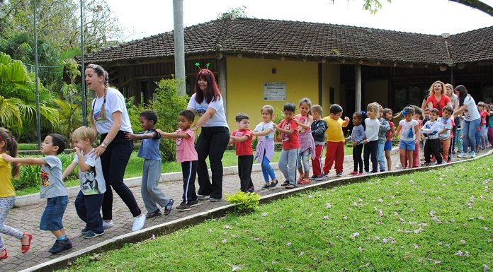 alunos e professoras fazem um trenzinho em área esterna com gramado da escola do meio ambiente