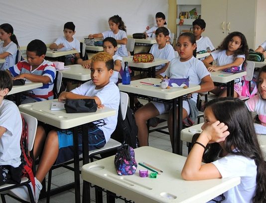 crianças sentadas em carteiras numa sala de aula