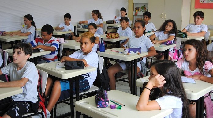 crianças sentadas em carteiras numa sala de aula