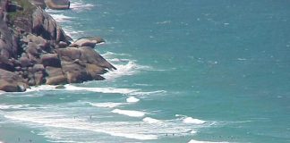 foto de uma praia em dia ensolarado com muitos banhistas vista de cima e de longe, como que de um prédio