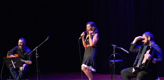 trio no palco; bia está em pé no meio dando risada