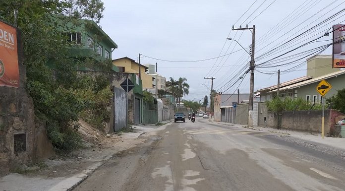 rua em que houve obra com parte de asfalto e outra de terra; carros ao fundo e casas ao lado
