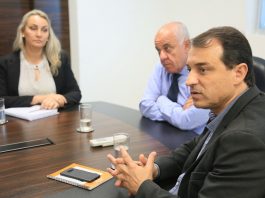 moisés, daniela e dado cherem sentado na ponta de uma mesa; carlos moisés está falando e gesticulando