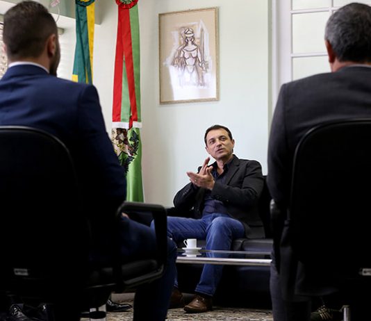 moisés é visto falando sentado em um sofá observado por dois homens sentado em outras poltronas