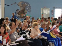 Conferência municipal da pessoa idosa abordou desafios do envelhecimento pessoas idosas sentadas na plateia com os braços levantados