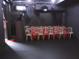 cadeiras de plásticos dispostas para plateia dentro de uma sala totalmente preta para o teatro