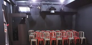 cadeiras de plásticos dispostas para plateia dentro de uma sala totalmente preta para o teatro