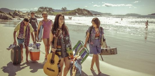 cena do filme em que as pessoas estão andando na praia carregando malas de viagem